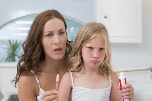 woman and young girl in bathroom frowning as they prepare to brush teeth