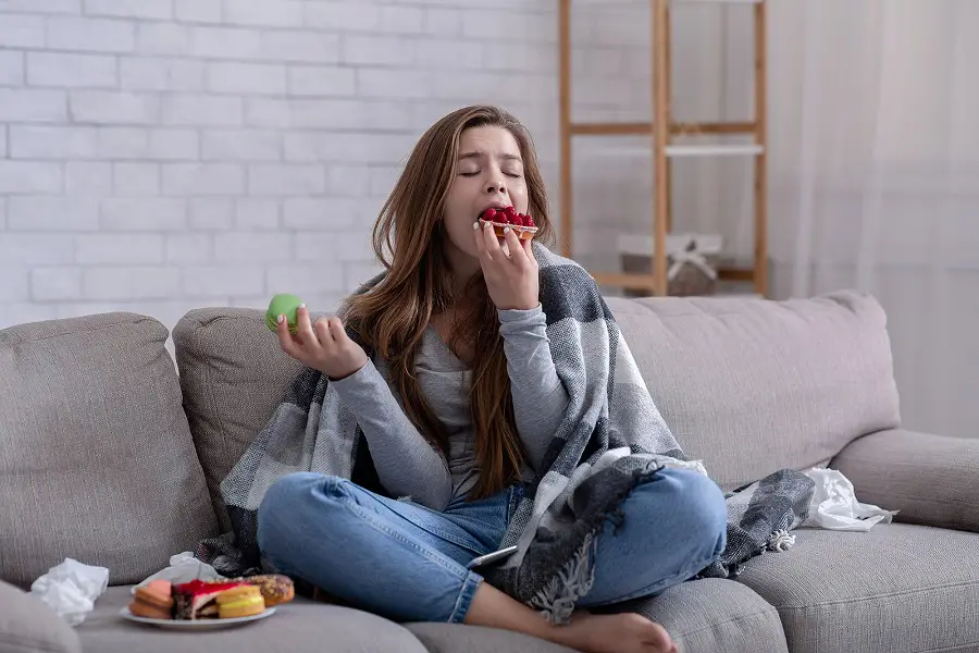 woman on sofa eating plate full of sweets