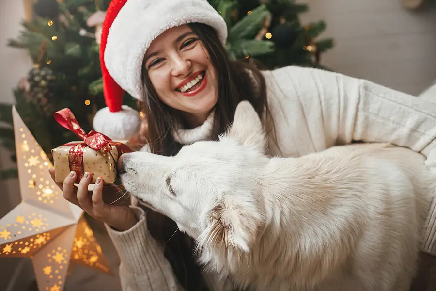 woman smiling holding present in front of christmas tree